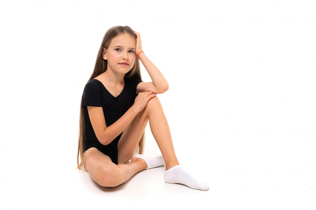 Garota ginasta sentado no chão sobre um fundo branco, com espaço de cópia