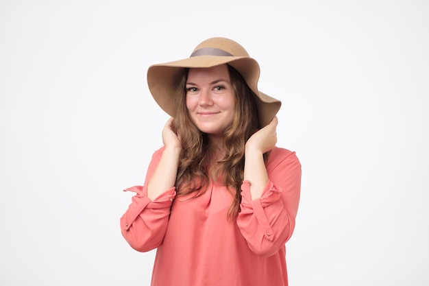 Garota gorda caucasiana sorridente em um chapéu com maquiagem natural e camisa vermelha olhando para a câmera Ela está curtindo a vida