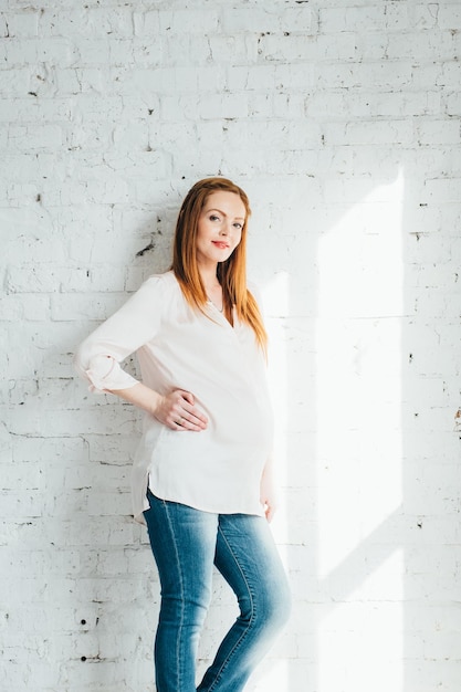 Garota grávida ruiva em uma blusa leve e jeans azul