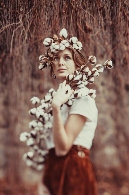 Garota incrível com olhos azuis, com penteado de moda com flores de algodão.