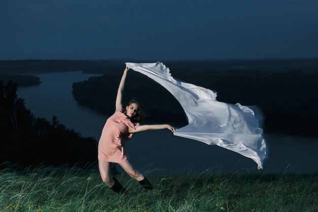 Garota incrível dançando no vestido rosa com grande xale branco à noite