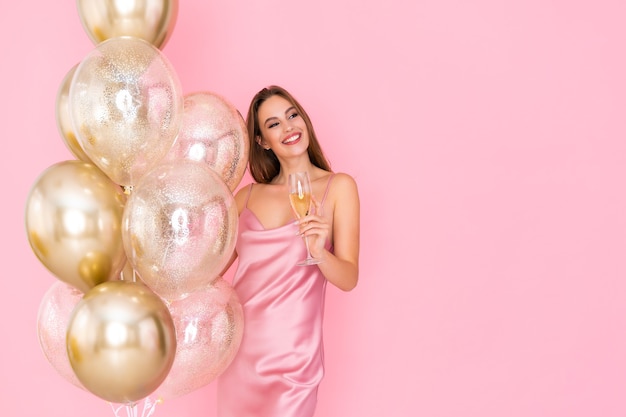 Garota incrível e feliz segurando uma taça de champanhe e muitos balões de ar vieram para a celebração da festa