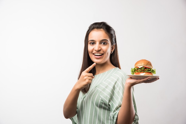 Garota indiana asiática atraente comendo hambúrguer em fundo branco ou amarelo