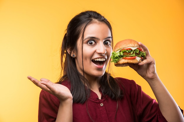 Garota indiana asiática atraente comendo hambúrguer em fundo branco ou amarelo