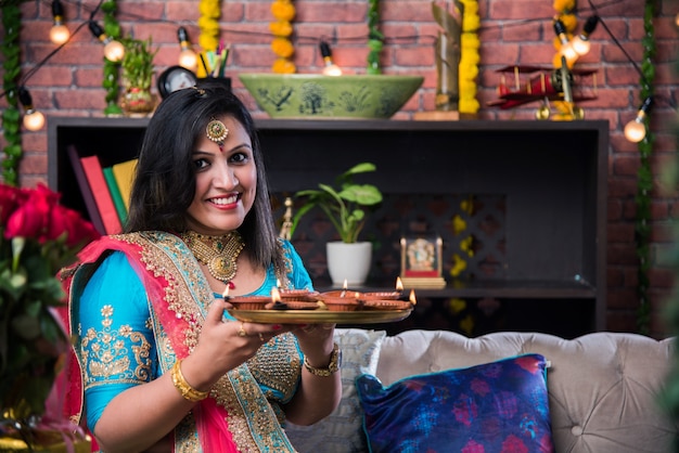 Garota indiana segurando diwali diya com roupas tradicionais, clicando na imagem de selfie ou falando pelo smartphone.