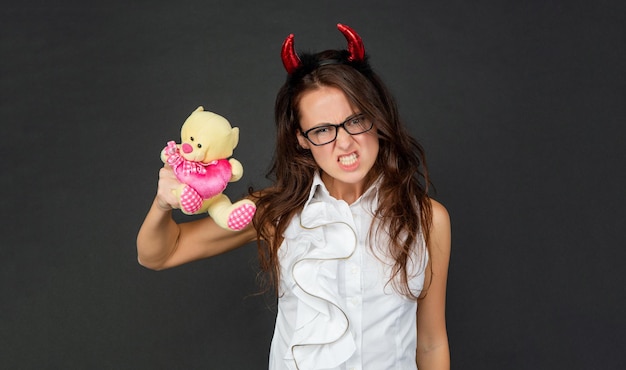 Garota irritada com chifres de diabo vermelho faz cara assustadora segurando o dia dos namorados tem fundo escuro, Halloween.