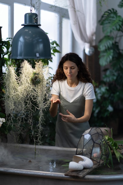 Garota jardineira cuidando de plantas aquáticas em estufa segurando plantas de casa sob banho com água