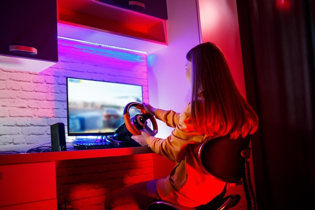 Garota jogadora jogando corrida em um computador Ela usa um volante de jogo emocional