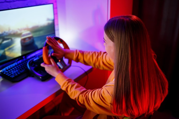 Garota jogadora jogando corrida em um computador Ela usa um volante de jogo emocional