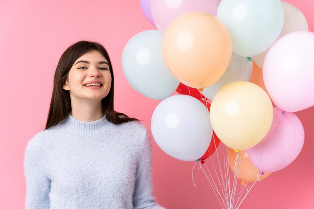 Garota jovem adolescente segurando muitos balões sobre parede rosa