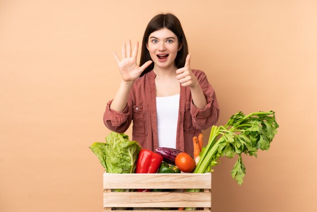 Garota jovem agricultor com legumes recém colhidos em uma caixa contando seis com os dedos