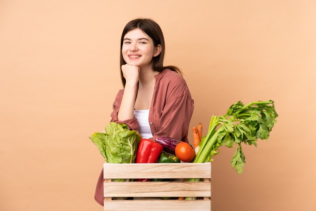 Garota jovem agricultor com legumes recém colhidos em uma caixa feliz e sorridente