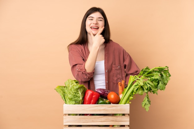 Garota jovem agricultor com legumes recém colhidos em uma caixa sorrindo