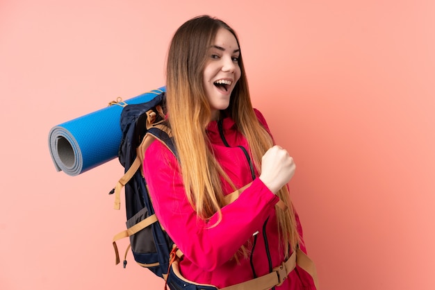 Garota jovem alpinista com uma mochila grande na parede rosa comemorando uma vitória