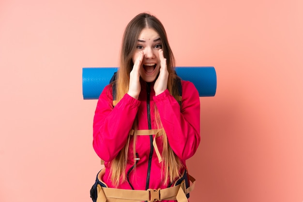 Garota jovem alpinista com uma mochila grande na parede rosa gritando com a boca aberta