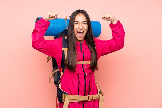 Garota jovem alpinista com uma mochila grande rosa comemorando uma vitória