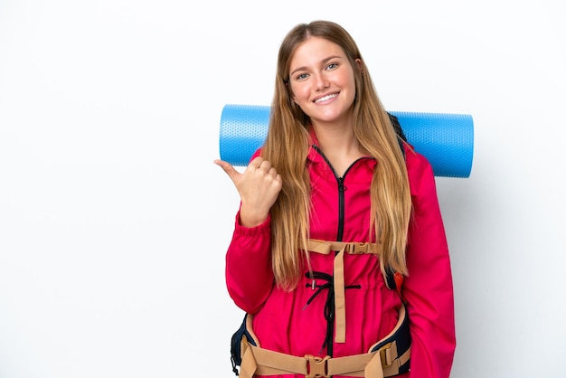 Garota jovem alpinista com uma mochila grande sobre fundo branco isolado, apontando para o lado para apresentar um produto