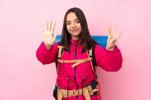 Garota jovem alpinista com uma mochila grande sobre parede rosa isolada, contando nove com os dedos