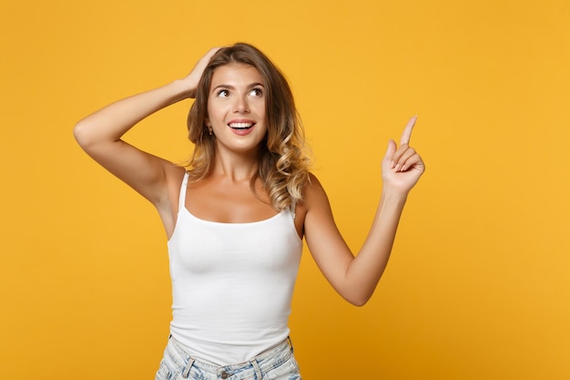 Garota jovem animada em roupas casuais leves posando isolado no fundo da parede laranja amarela. conceito de estilo de vida de pessoas. mock up espaço de cópia. colocando a mão na cabeça, apontando o dedo indicador para cima.