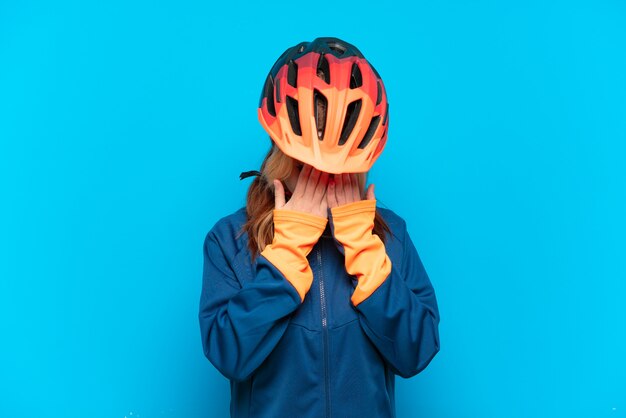 Garota jovem ciclista isolada em um fundo azul com uma expressão cansada e doente