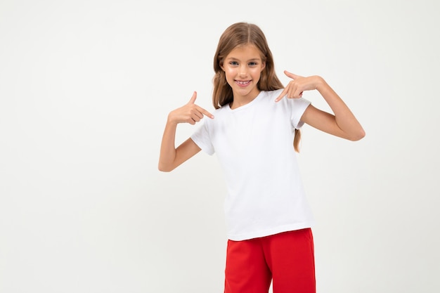 Garota jovem e atraente caucasiana em uma camiseta branca com um layout e calça vermelha em branco