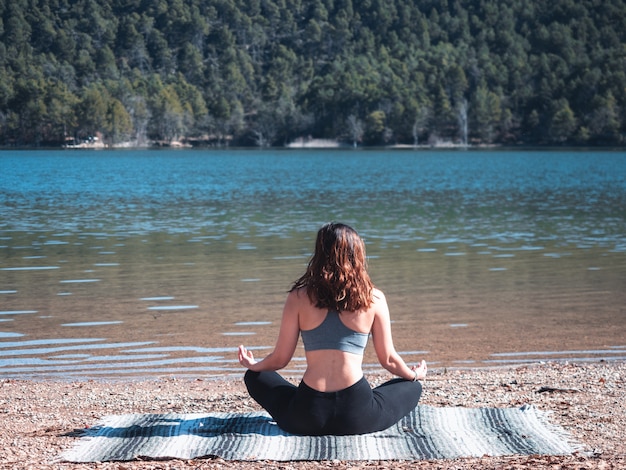 Garota jovem e atraente fazendo yoga ao ar livre, ao lado de um lago, rodeado pela natureza. conceito de vida saudável.