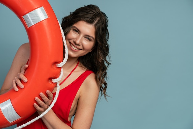 Garota jovem e atraente posando com uma bóia salva-vidas em um fundo azul. Linda garota em um espaço de cópia