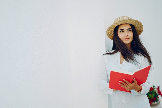 garota jovem e bonita em uma cidade de verão em pé perto da parede branca com livro vermelho
