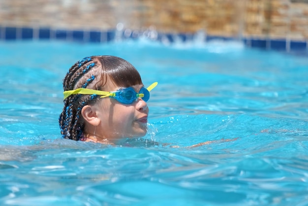 Garota jovem em óculos de exercícios nadando na água azul da piscina Conceito de atividade de recreação de verão