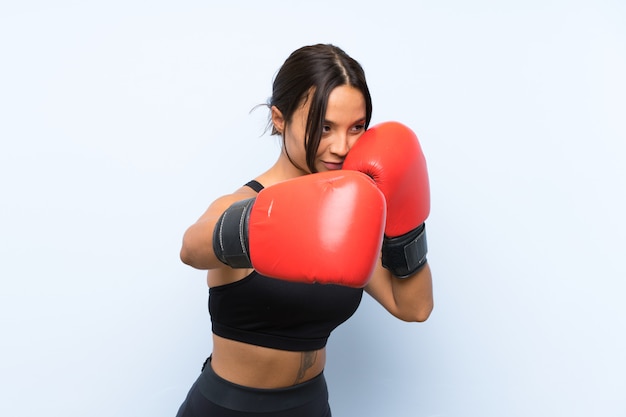 Garota jovem esporte com luvas de boxe sobre fundo azul isolado