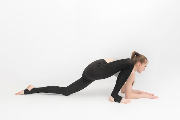 Garota jovem ginasta esbelta faz um exercício para desenvolver flexibilidade em fundo branco. Asanas na ioga.