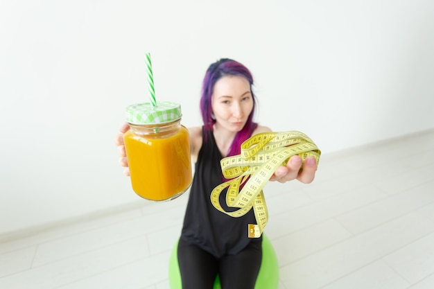 Garota jovem hippie embaçada com cabelo colorido segurando um smoothie de proteína de banana e fita métrica