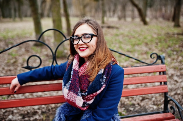 Garota jovem hippie veste um casaco e óculos, sentado no banco