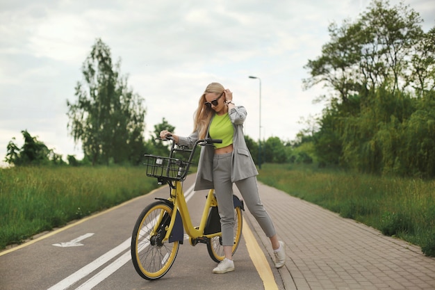 Garota jovem modelo com roupas da moda posando com uma bicicleta amarela na ciclovia