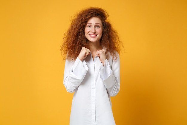 Garota jovem ruiva sorridente alegre em uma camisa branca casual posando isolada em uma parede laranja amarela