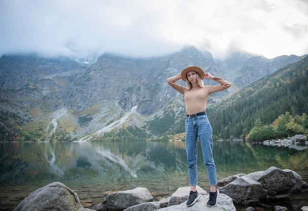 Garota jovem turista de chapéu com as mãos no topo das montanhas admira a natureza