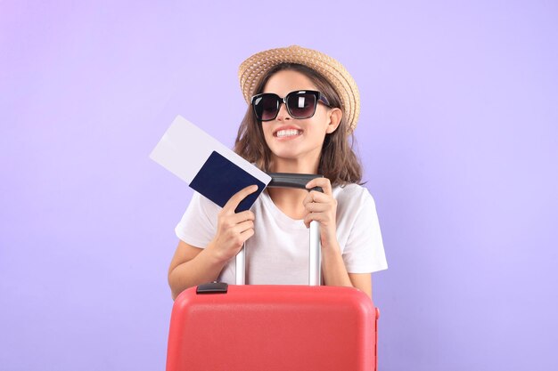 Garota jovem turista em roupas casuais de verão, com óculos de sol, mala vermelha, passaporte isolado em fundo roxo