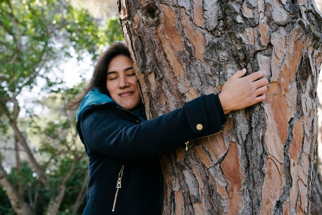Garota latina abraçando uma árvore na natureza enquanto sorria e meditava em contato com a natureza