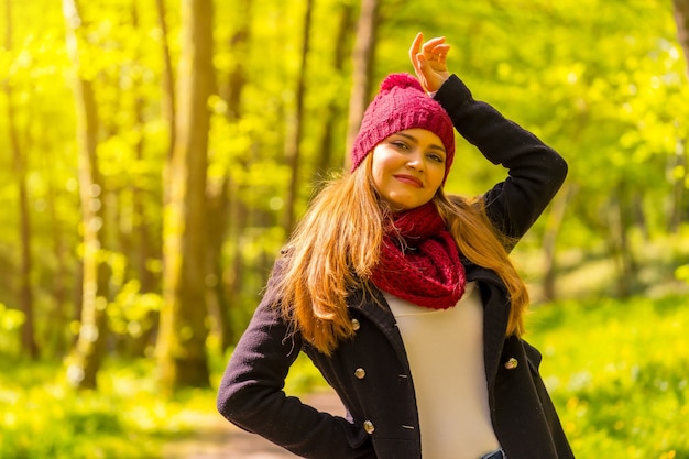 Garota latina com uma jaqueta preta, lenço e chapéu de lã vermelha curtindo em um parque no outono, sorrindo, olhando para a câmera