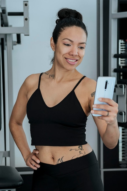 Garota latina e esportiva usando seu celular na academia olhando suas mensagens ou redes sociais