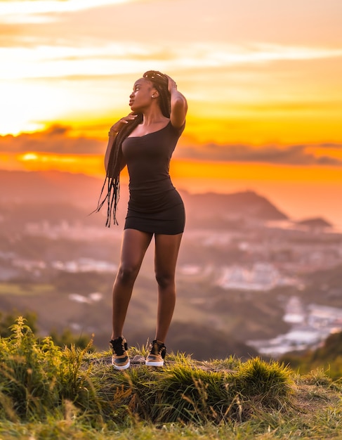 Foto garota latina estilo de vida com pele negra com lindas tranças longas no cabelo e um vestido preto curto e apertado