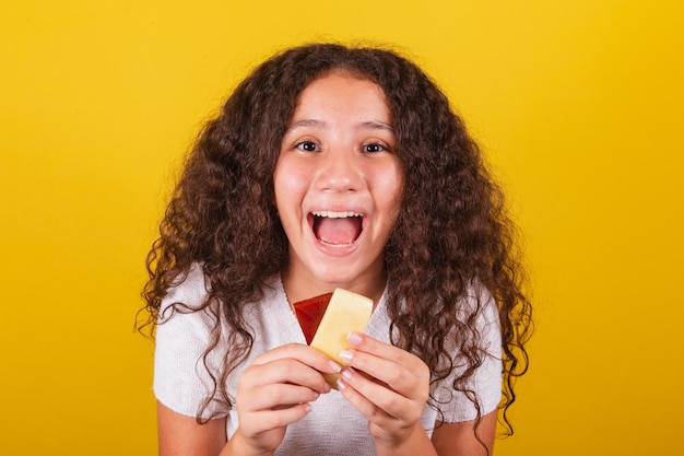 Garota latino-americana afro-brasileira com cabelos cacheados sorrindo segurando espetos de queijo e goiaba e pedaço de queijo e goiaba apetitoso desejo romeu e julieta doce delicioso