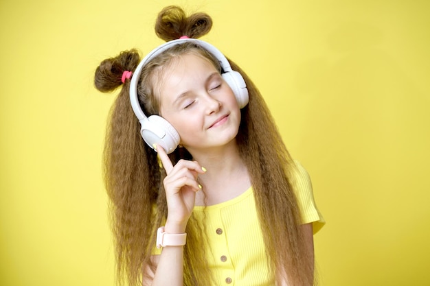 Garota legal e bonita com penteado moderno em fones de ouvido ouve música em fundo amarelo