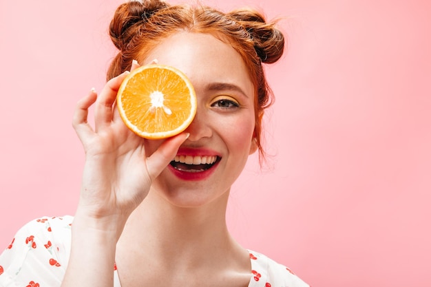 Garota legal em camiseta branca cobre os olhos com metades laranja e sorri no fundo rosa