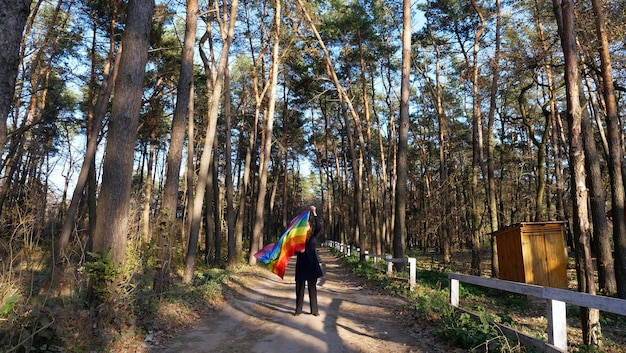 Garota lésbica bissexual segurando uma bandeira LGBT arco-íris na floresta no mês do orgulho