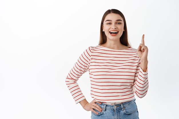 Garota linda e feliz promovendo a loja, apontando o dedo para cima, mostrando o anúncio para cima, copie o espaço, aponta para algo, em pé sobre um fundo branco