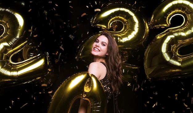 Garota linda feliz em um vestido de festa sexy elegante segurando balões de ouro 2022, se divertindo na festa de Natal ou Ano Novo.