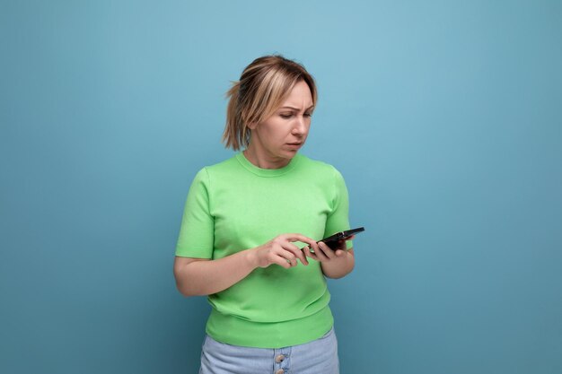 Garota loira atraente duvidosa segurando um smartphone na mão em um fundo azul com espaço de cópia