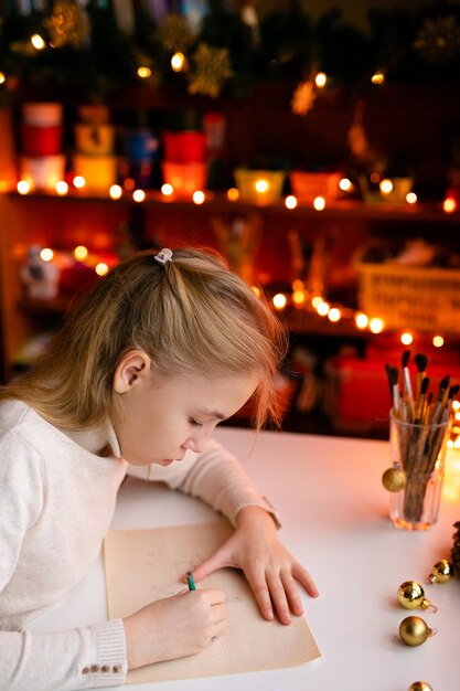 Garota loira criança escrevendo a carta para o Papai Noel ou algo de desenho na com bokeh amarelo quente