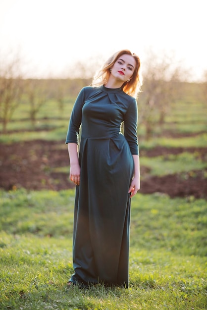 Garota loira de elegância Yong no vestido verde no jardim na primavera no pôr do sol